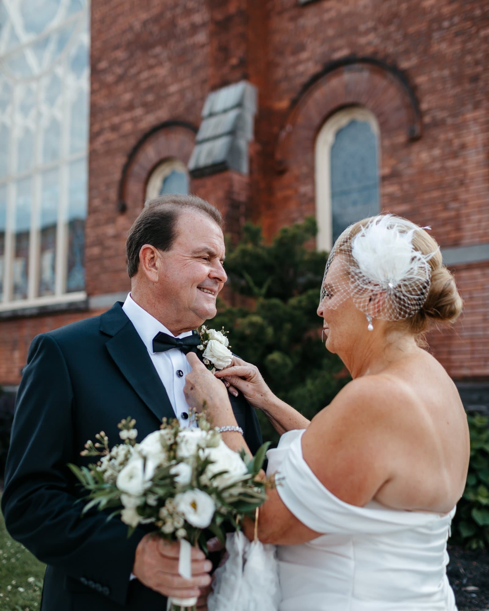 Bride pinning a boutonnière on the groom outside a historic brick church