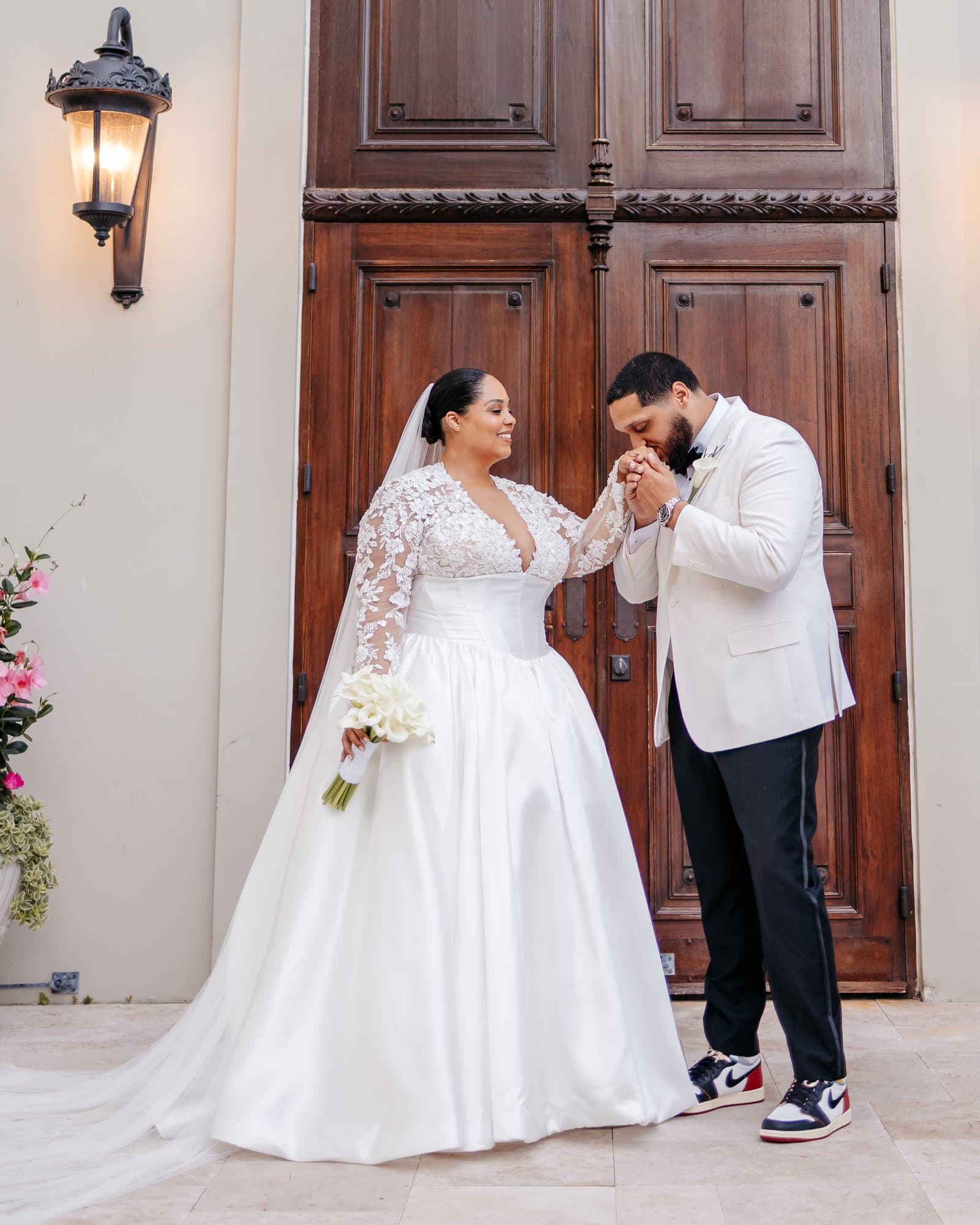 Groom kissing the bride's hand in front of carved wooden doors