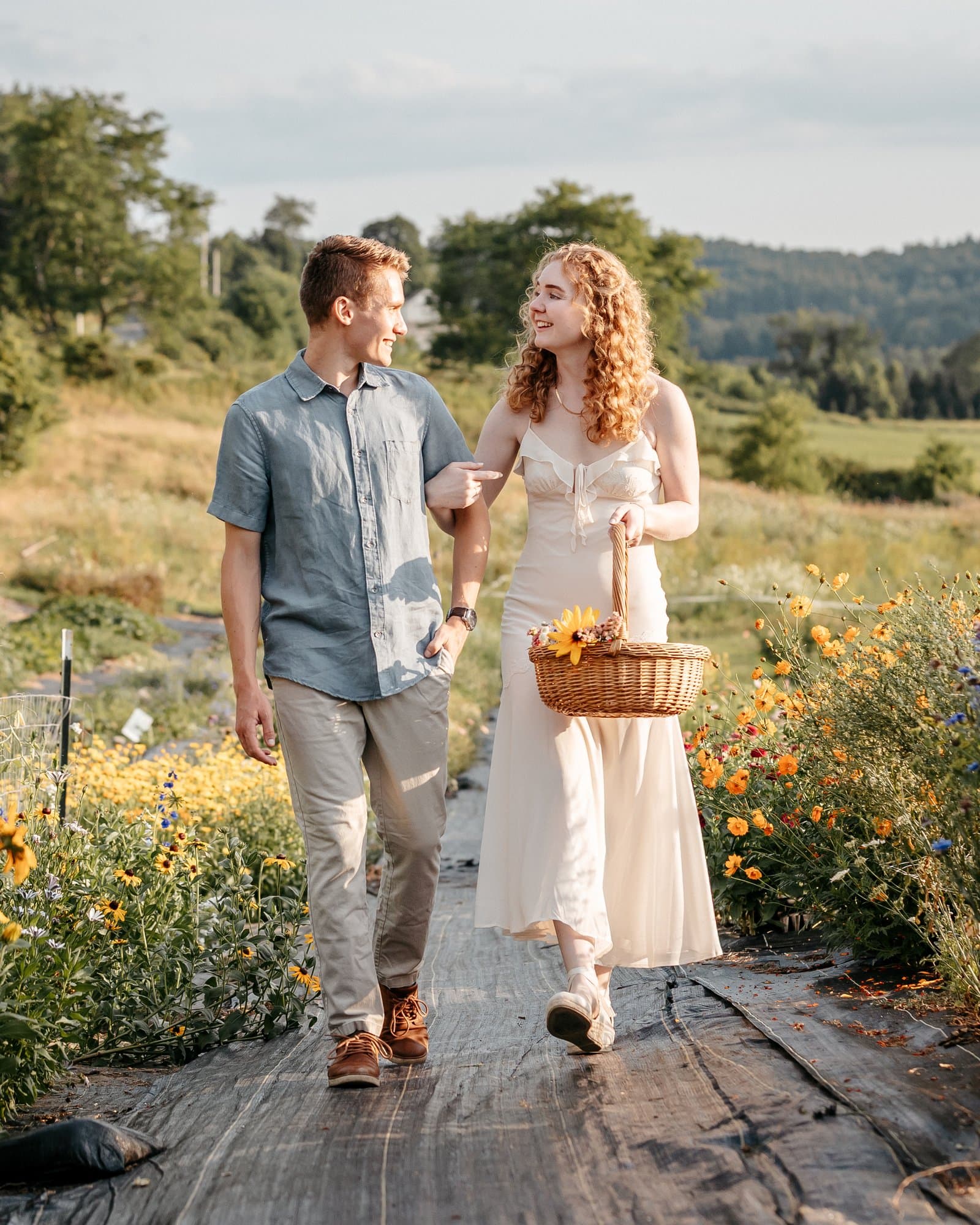 Engaged couple walking arm in arm through a flower farm at golden hour
