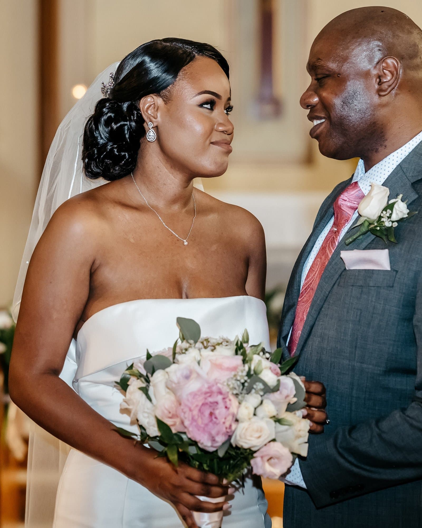 Bride with a blush bouquet smiling at the groom inside a candlelit church