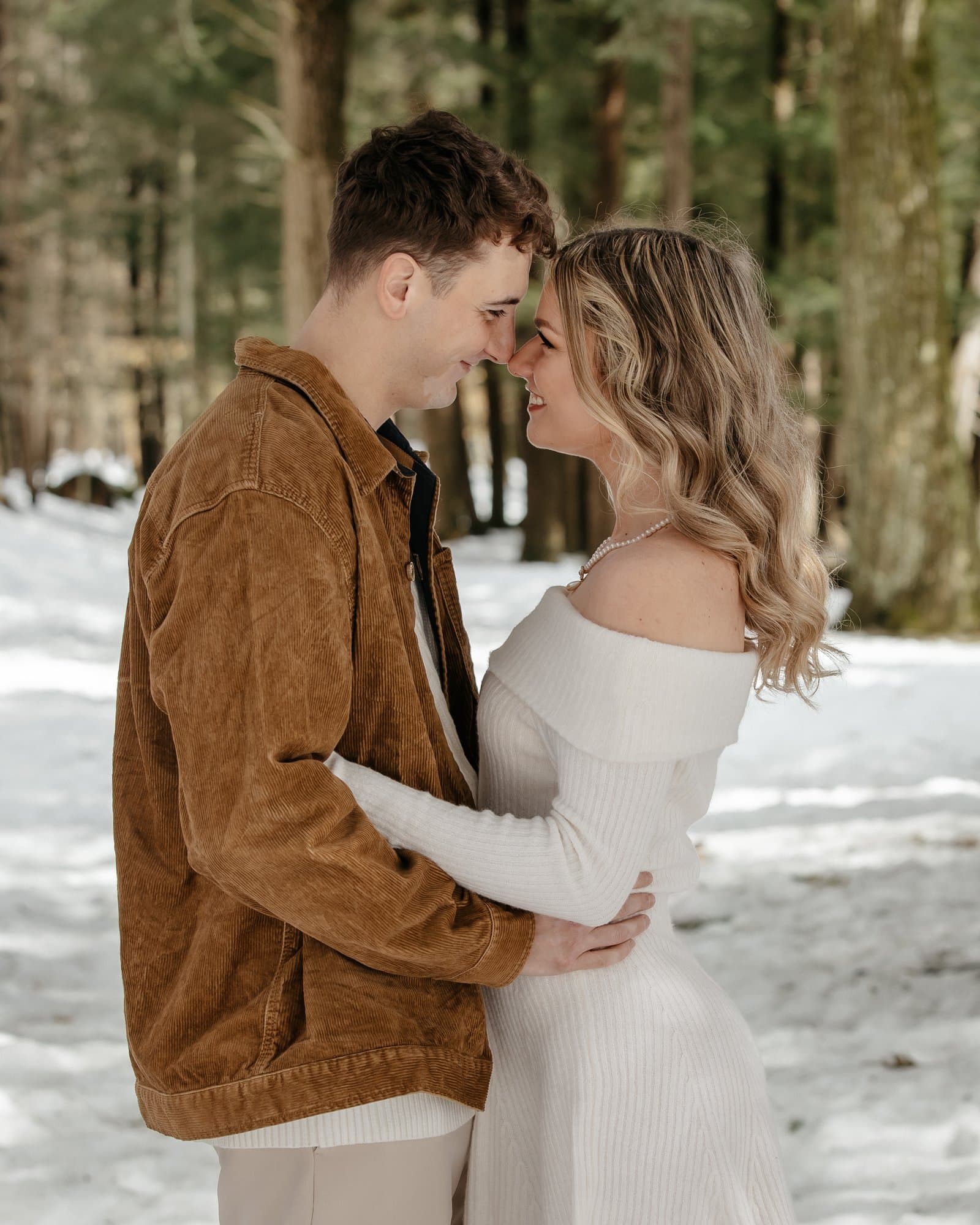 Engaged couple nose to nose in a snowy pine forest