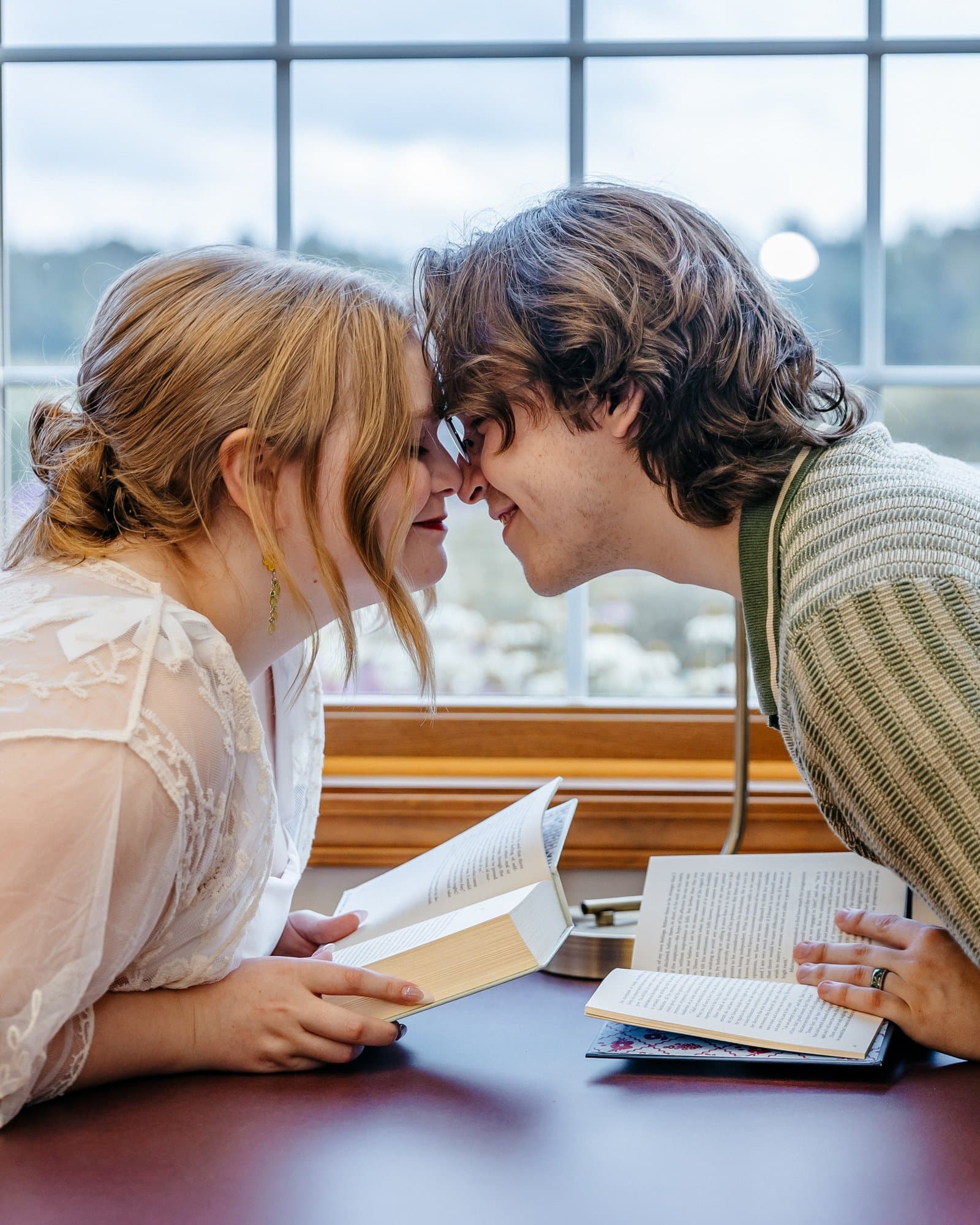 Couple touching noses over open books in a library reading nook