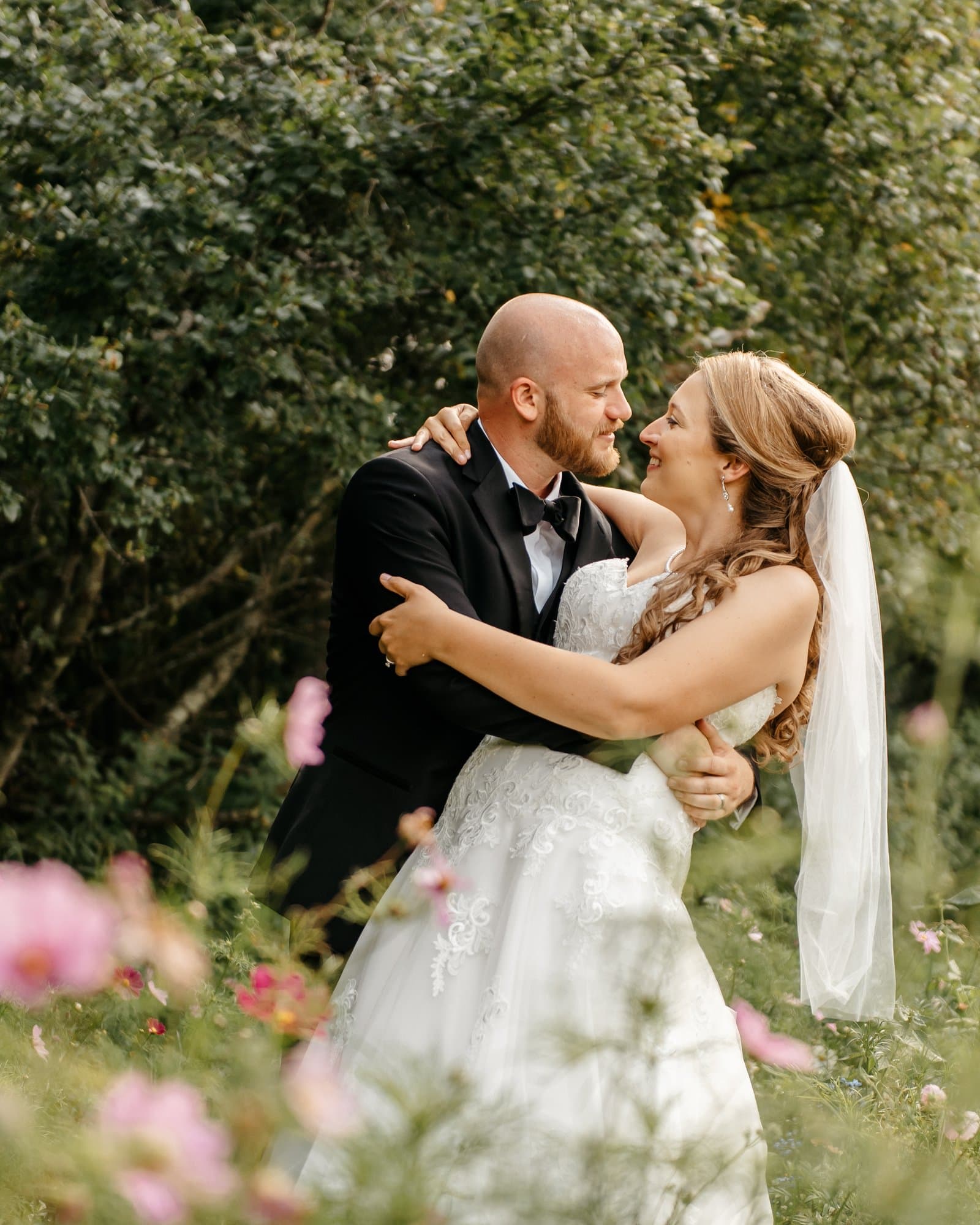 Groom embracing the bride in a field of pink cosmos flowers