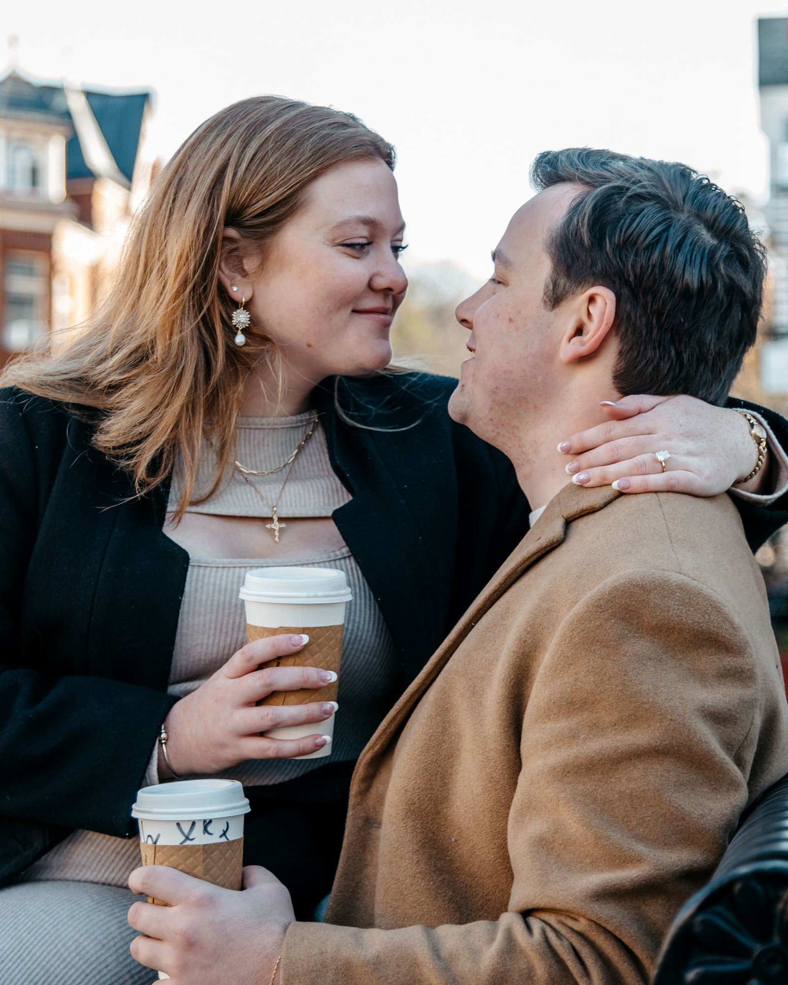 Engaged couple sharing coffee on a downtown bench in winter