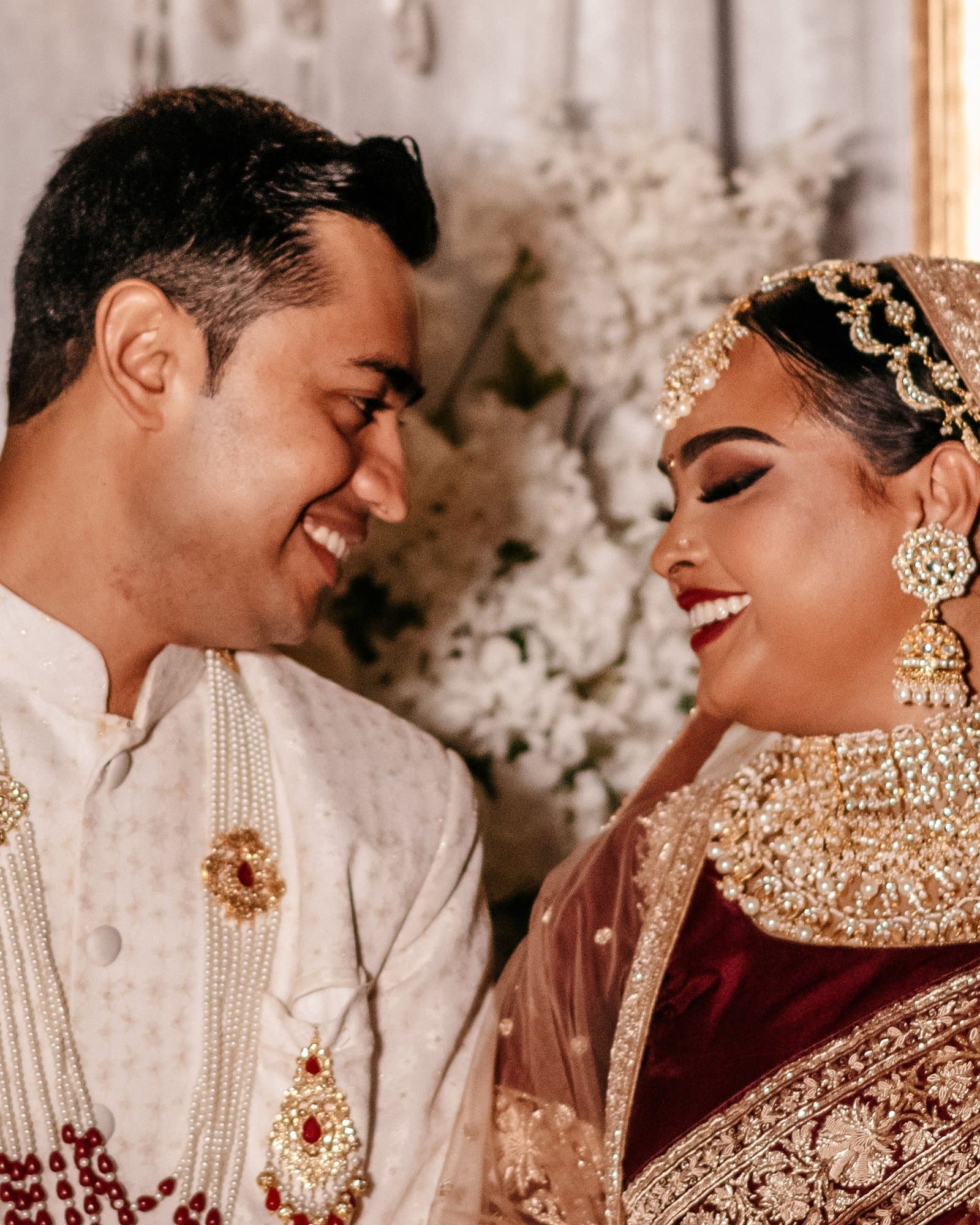 Bride and groom in traditional South Asian wedding attire smiling at each other