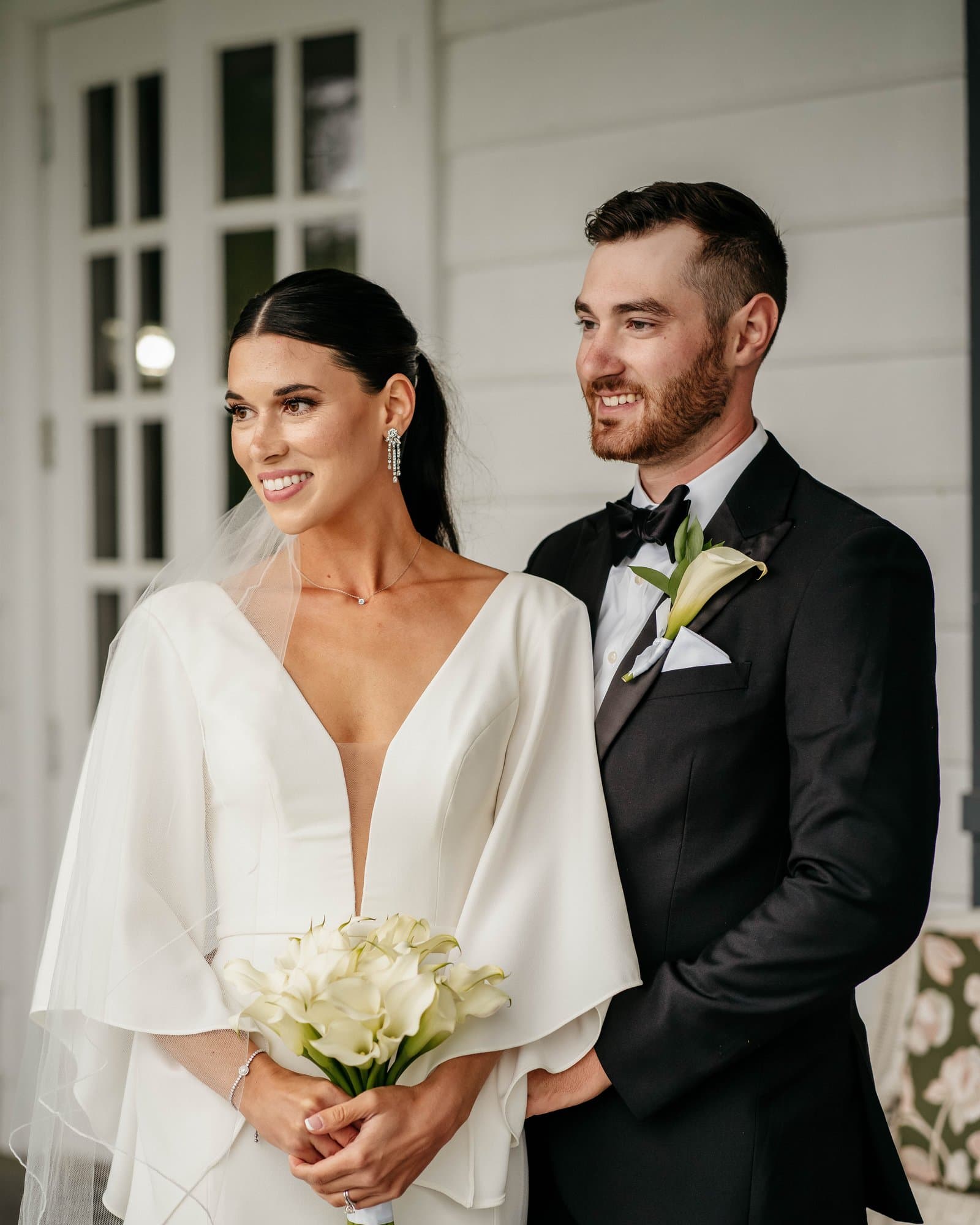 Bride holding calla lilies beside the groom on a white porch