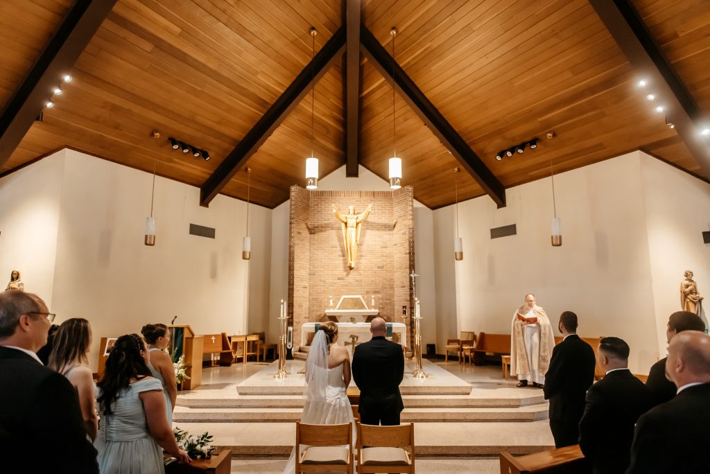 A bride and groom stand at the alter knowing how much to get married in new york surrounded by their friends and family in a catholic church