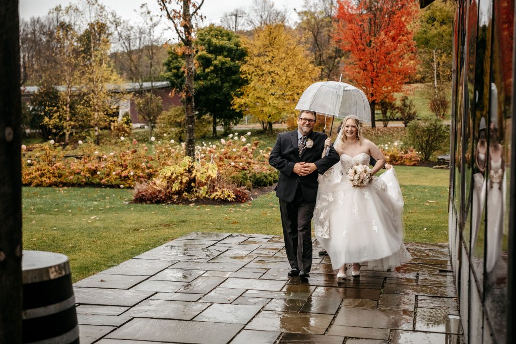 A bride and her father walk toward her wedding in the rain at Gables and Gardens