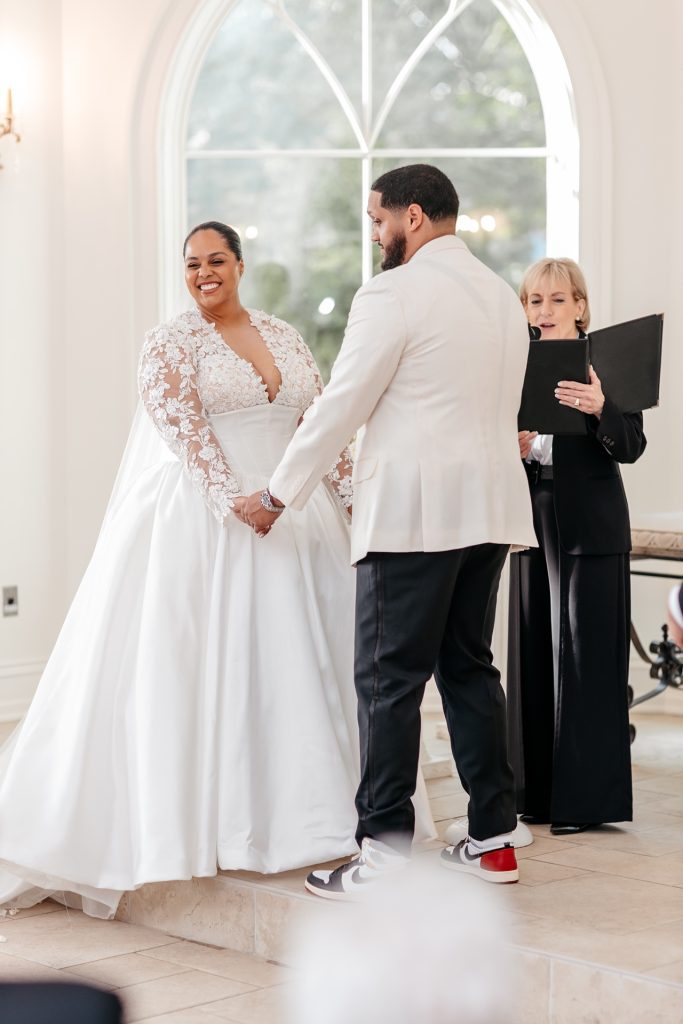 A bride and groom smile while holding hands and looking at their family during their new york wedding photo